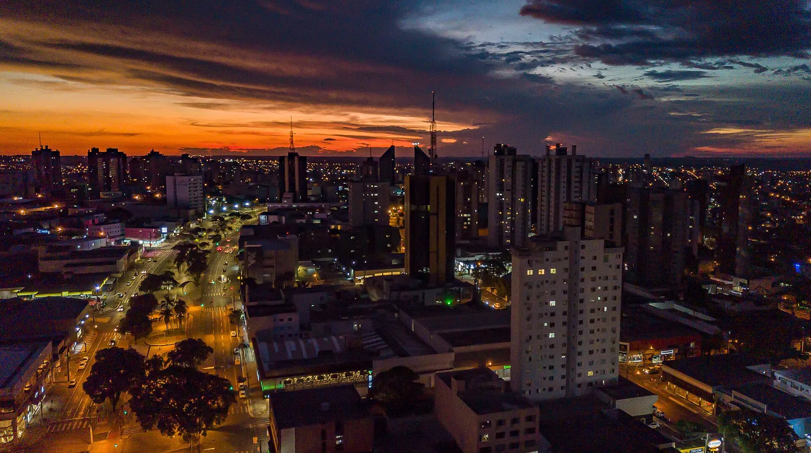 Vista aérea do centro de Cascavel, no Paraná, ao entardecer, com avenida e edifícios iluminados