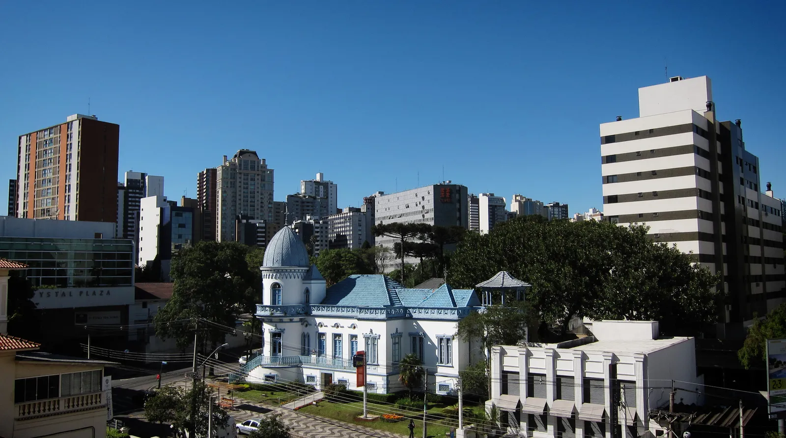 Bairro Batel, em Curitiba, com casarão azul e branco em primeiro plano e prédios ao fundo