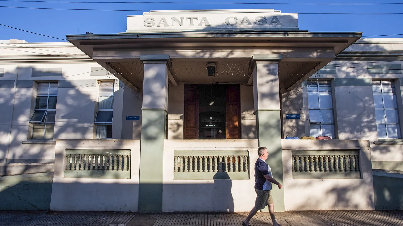 Fachada da Santa Casa de São Carlos, com a palavra Santa Casa no frontão e um pedestre na calçada