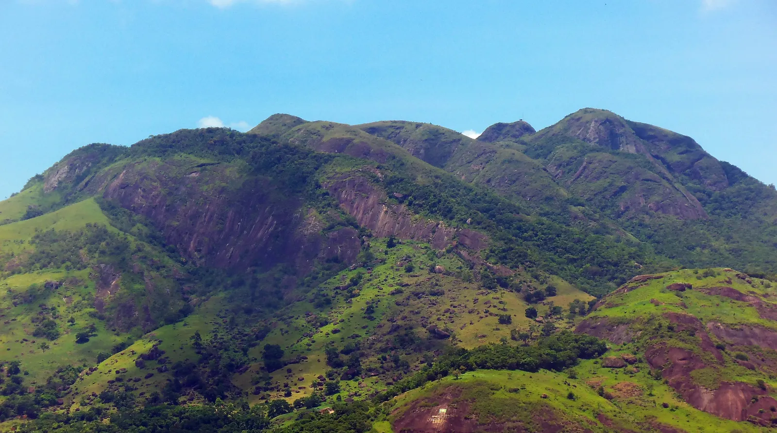 Morro Mestre Álvaro, na Serra (ES), com encostas verdes e paredões de rocha sob céu azul